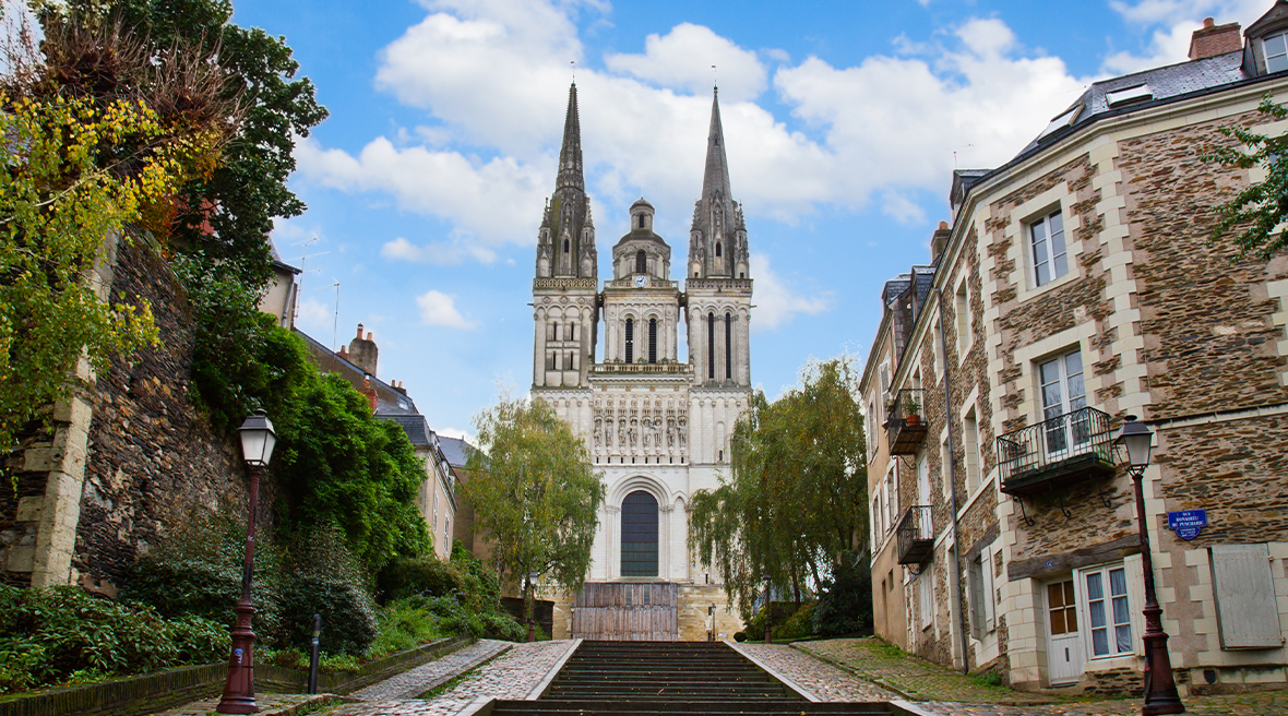 A cathedral with two spires and a bell tower stands at the top of a wide set of steps on a cobbled street uphill